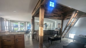 Amplia sala de estar con techo de madera, un sofá, una mesita de centro y una zona de cocina con armarios de madera.