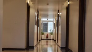 A long, well-lit hallway with a shiny floor, flanked by walls with framed pictures and potted plants. - Heritage Inn (Mysore)