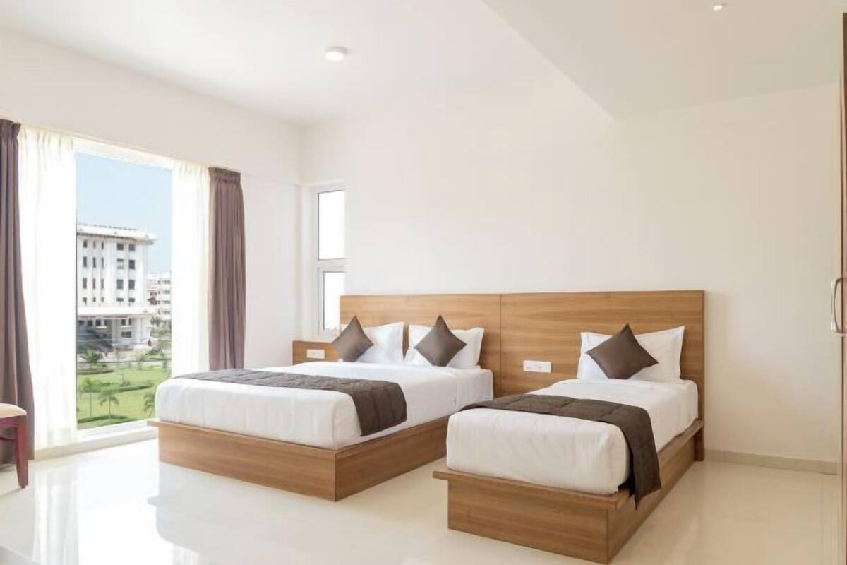 Une chambre d’hôtel moderne avec deux lits, une grande fenêtre avec des rideaux et une vue sur les bâtiments environnants.