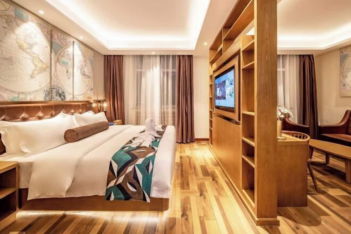 A hotel room with a large bed, a television, a wooden wardrobe, and a map on the wall.