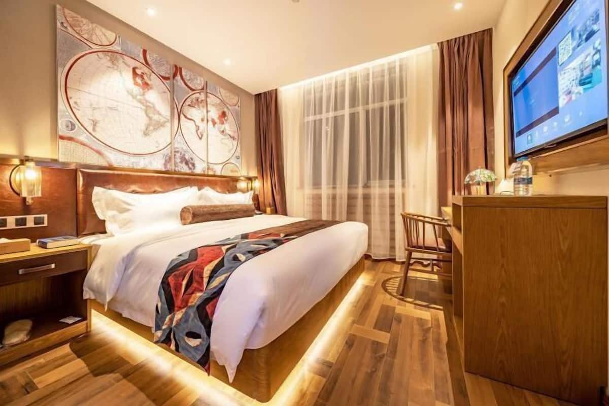A hotel room with a large bed, a desk, a TV, and a map on the wall.