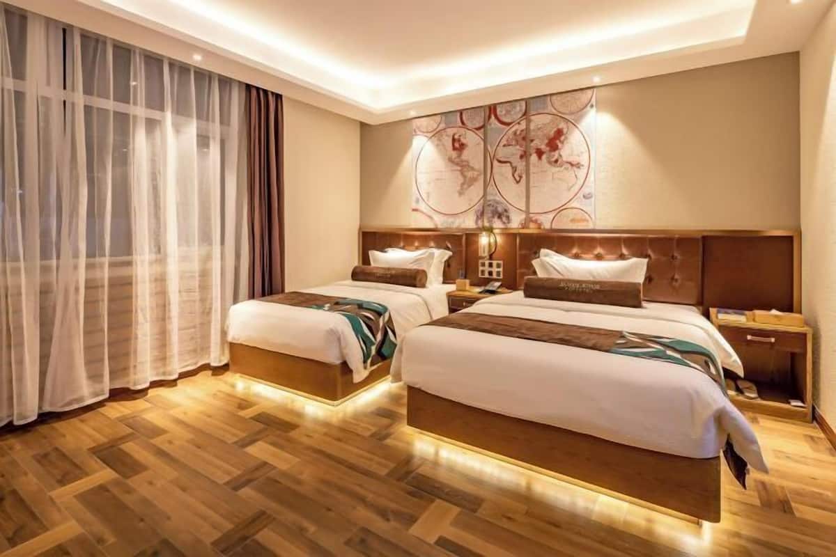A hotel room with two beds, a large window with sheer curtains, a world map on the wall, and a wooden floor.