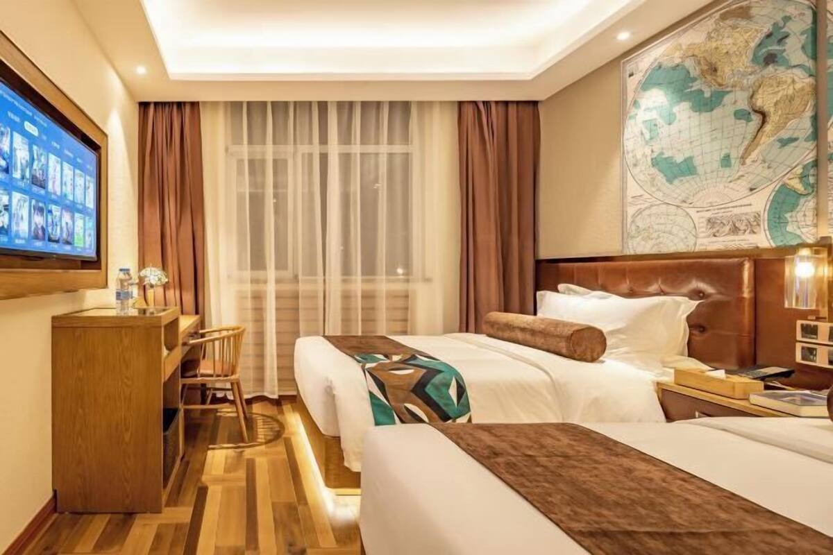 A hotel room with a bed, a desk, a TV, a map on the wall, and a window with curtains.