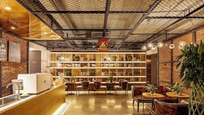 Un interior moderno con un mostrador de recepción de madera, una zona de estar y una estantería llena de libros y plantas.