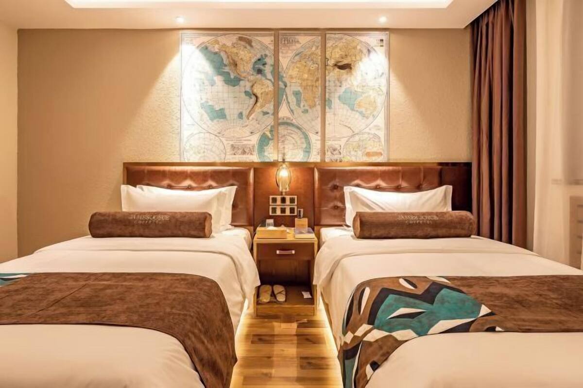 A hotel room with two beds, a large world map on the wall, and a wooden nightstand between the beds.