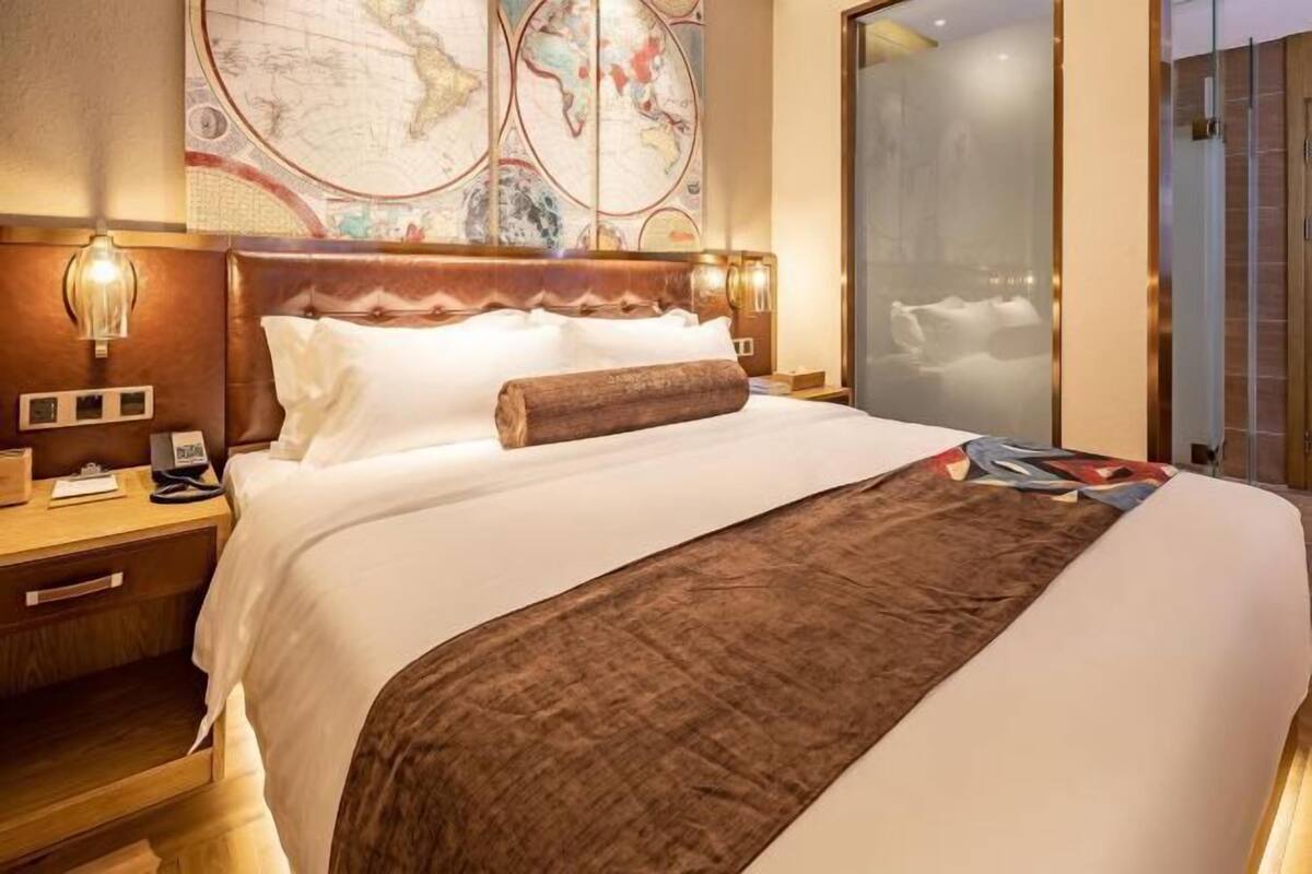 A hotel room with a large bed, a wooden headboard, a nightstand with a lamp, a map on the wall, and a sliding door leading to a bathroom.