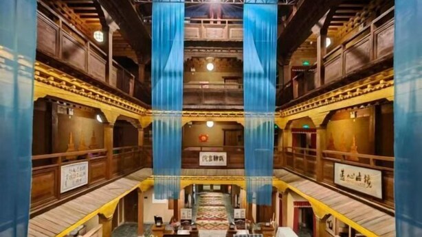 Una posada de madera tradicional con un corredor central, asientos a cuadros y cortinas azules colgantes.