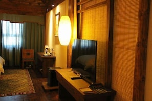 A hotel room with a wooden desk, a television, a lamp, a chair, and a bed with a headboard. - Shangri-La Fanyue Mountain Resort (Shangri-La)