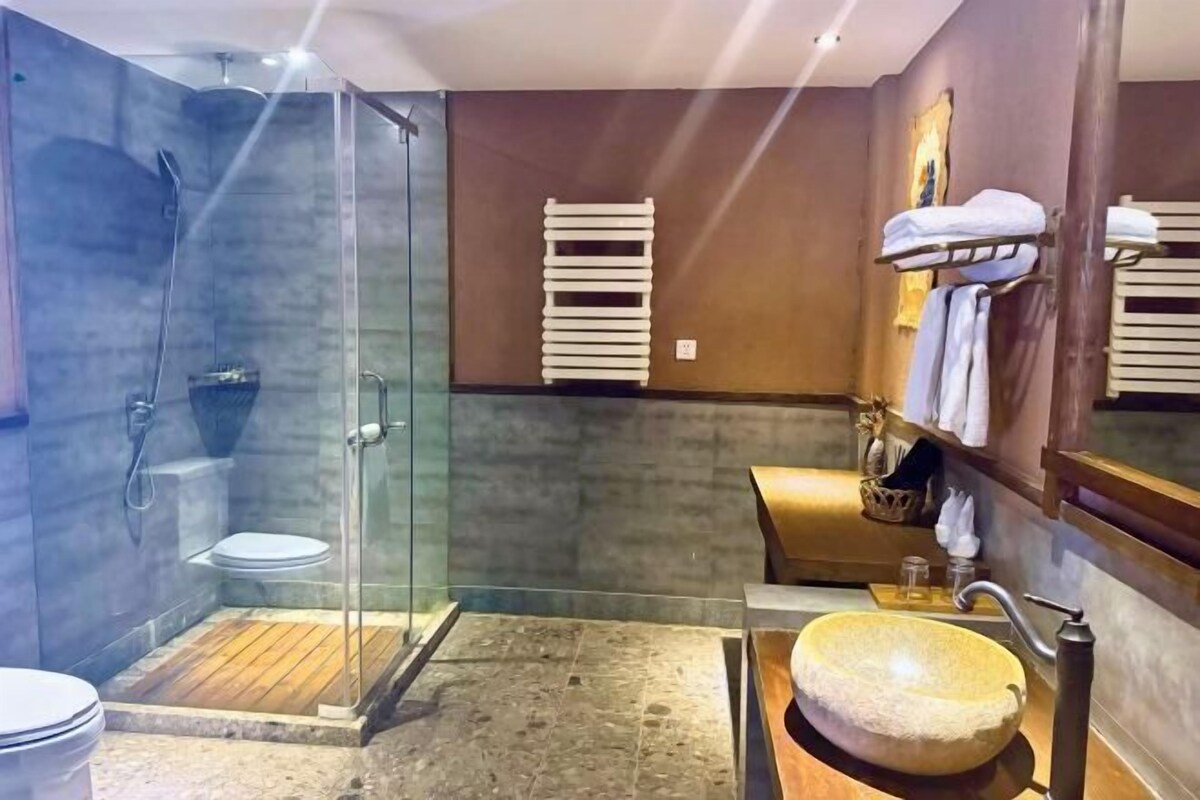 A bathroom with a glass-enclosed shower, a wooden vanity, and a large stone sink.