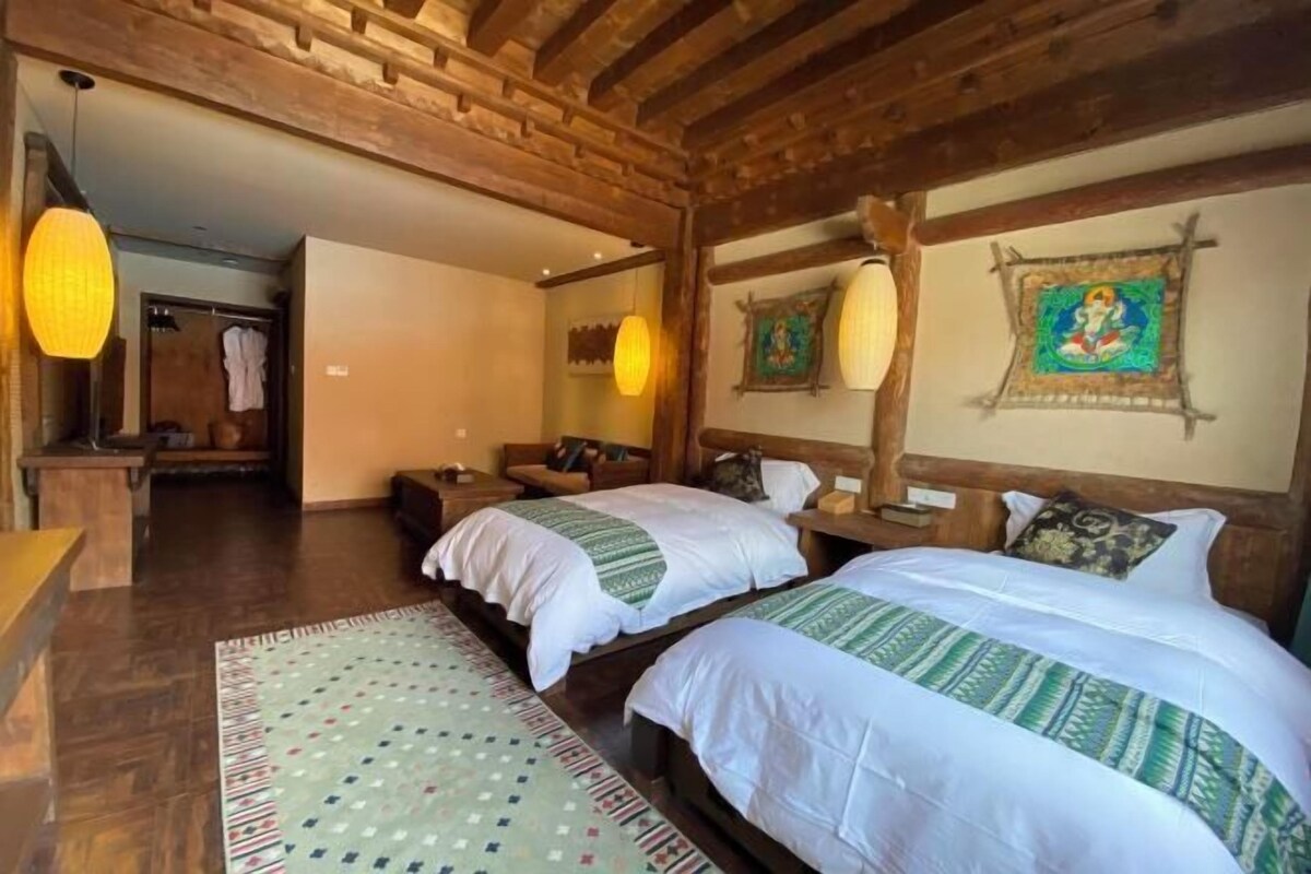 A room with two beds, wooden beams, hanging lamps, and a patterned rug.