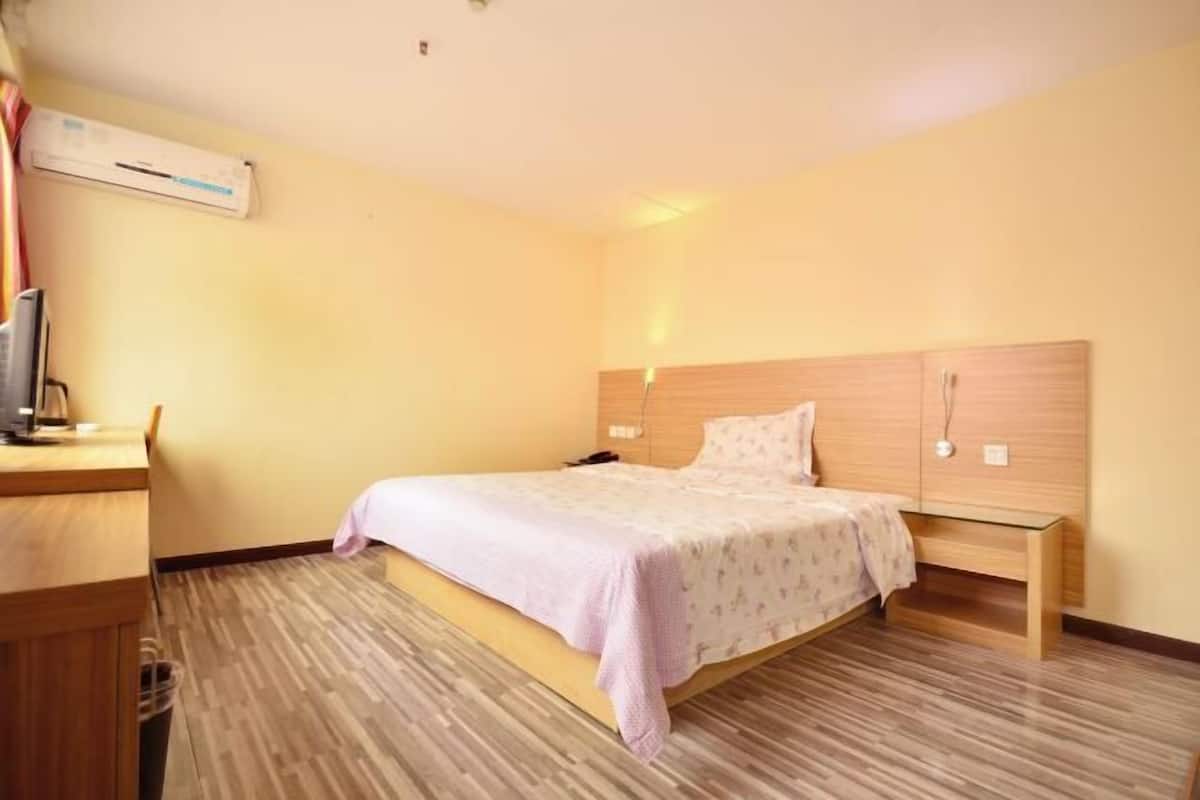 A hotel room with a bed, bedside table, and a desk with a chair.