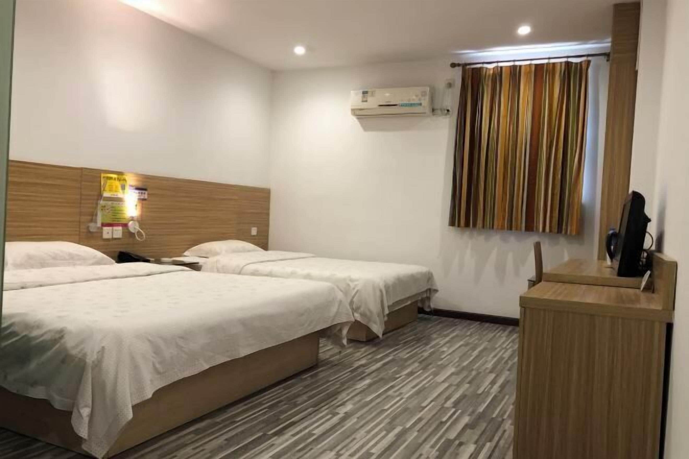 A hotel room with two single beds, a wooden headboard, an air conditioning unit, a striped curtain, and a wooden desk with a telephone.