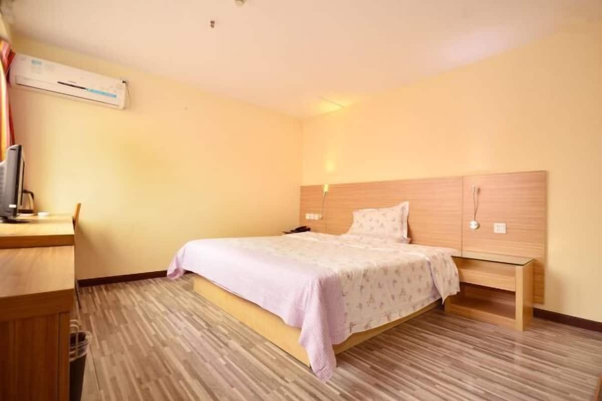A hotel room with a bed, bedside table, and a desk with a chair.