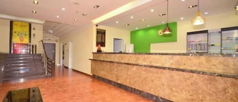 A hotel reception area with a marble counter, a green wall, and a staircase in the background.