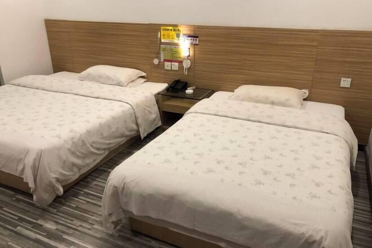 A hotel room with two beds, a wooden headboard, a bedside table with a phone, and a wall-mounted sign.