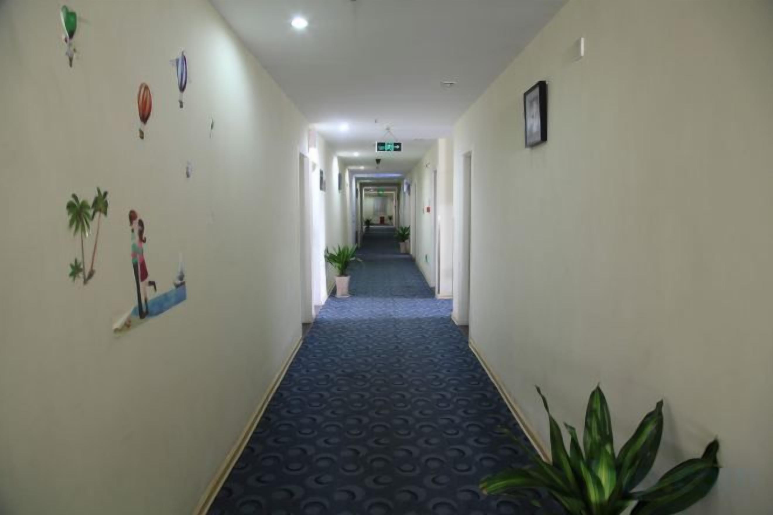 Pasillo de hotel con alfombra azul, decoraciones en la pared y plantas en macetas.