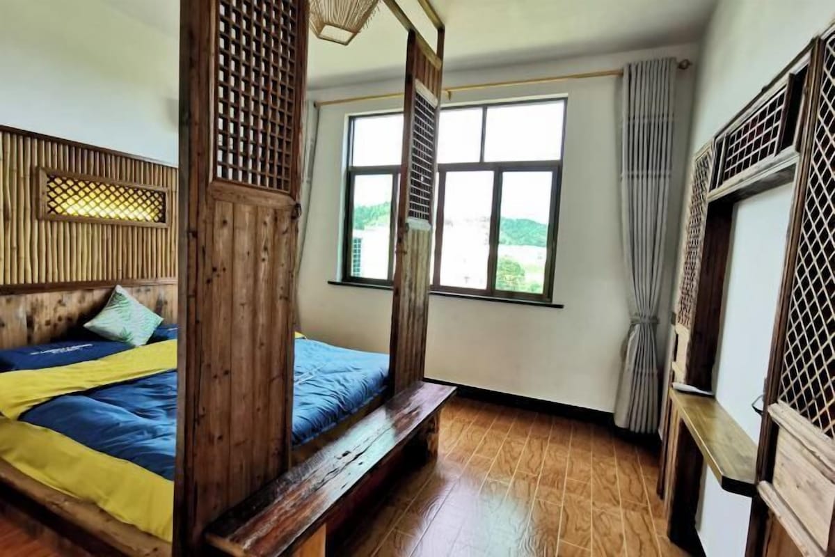 Quarto com cama de madeira, janelas amplas e vista para o verde.