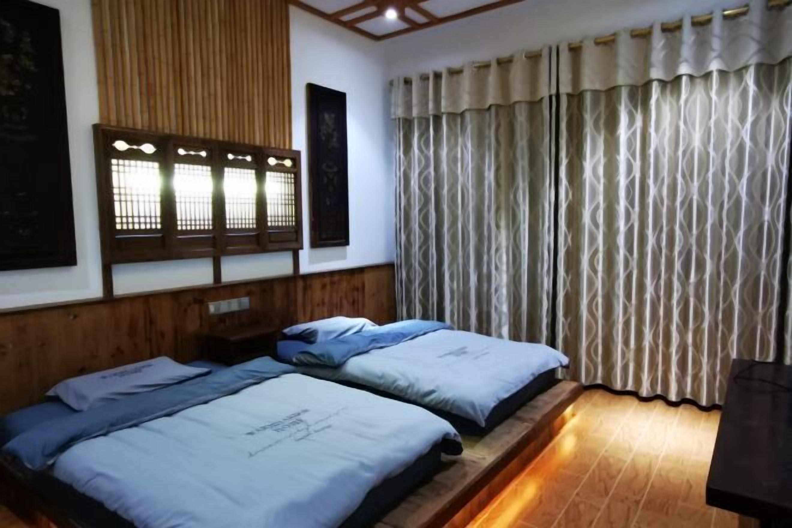 A room with two beds, a wooden headboard, a window with a traditional design, and a curtain.