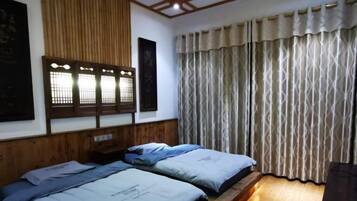 A room with two beds, a wooden headboard, a window with a traditional design, and a curtain.