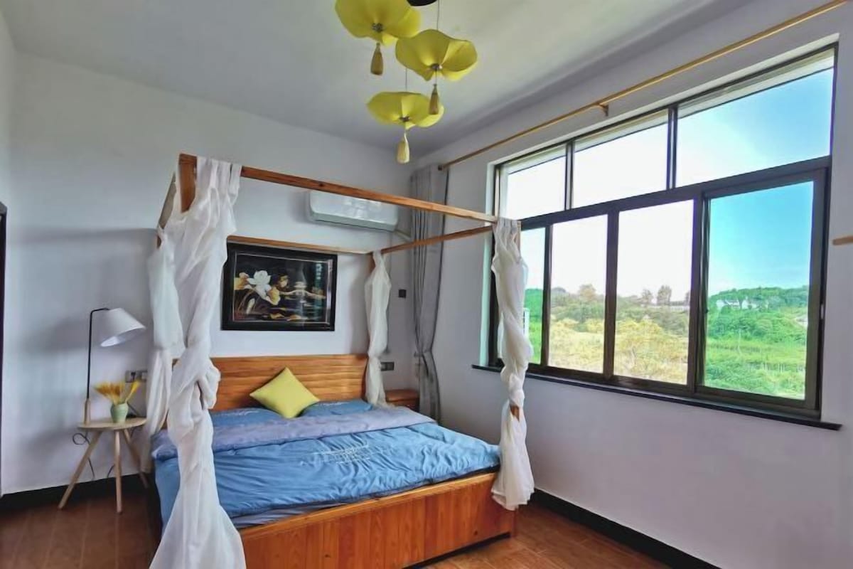 Quarto com cama de dossel, uma janela ampla com vista e mesa de cabeceira com luminária.