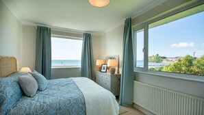 Ein Schlafzimmer mit Bett, Kommode, Lampe und Meerblick.