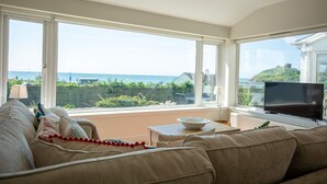 Ein Wohnzimmer mit großem Fenster und Blick auf das Meer und viel Grün.
