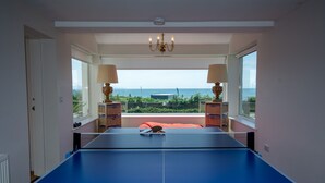 Ein Zimmer mit einem Tischtennisplatte, zwei Lampen, einer Kandelaber und Blick auf das Meer.