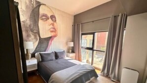 Un dormitorio con una cama grande, una mesita de noche, un calentador en la pared y una ventana con cortinas.