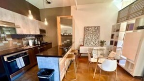 Una cocina moderna con una isla central, taburetes de bar y una zona de comedor con mesa y sillas.