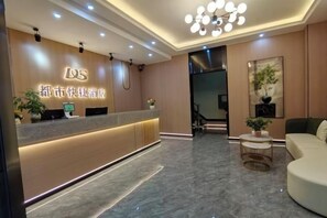 Zona de recepción de un hotel, con mostrador, área de descanso y escalera que sube a los pisos superiores.