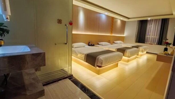 Habitación de hotel con ducha envuelta en vidrio, una cama grande con dos almohadas, una mesita de noche y vistas a la ciudad.