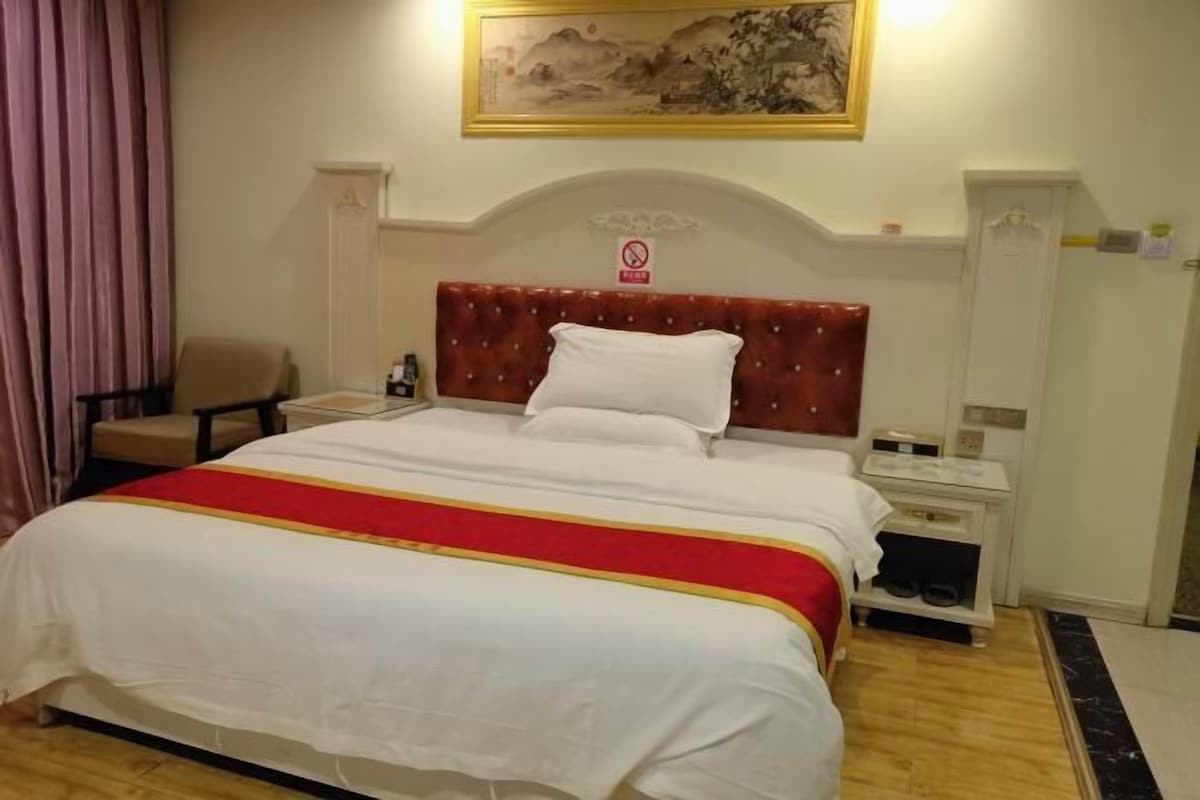 Una habitación de hotel con cama, mesita de noche, una silla, un cuadro en la pared y una puerta.