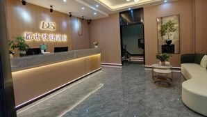Un área de recepción de hotel con diseño moderno, que incluye un mostrador de recepción, una zona de estar con un sofá y una escalera que conduce a otro piso.