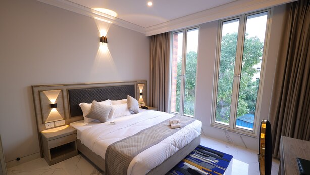 Quarto de hotel moderno com uma cama grande, luminárias de cabeceira, vista para áreas verdes e um espaço de refeições.