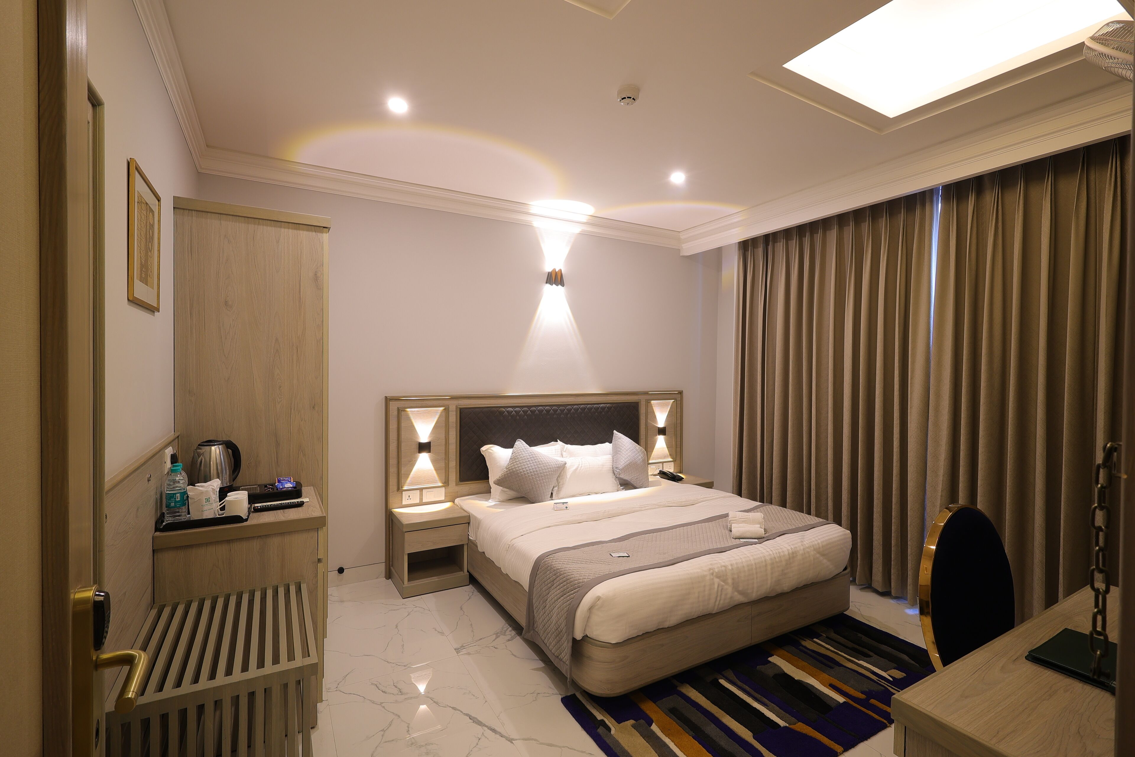 A hotel room with a bed, bedside tables, a desk, a chair, a wardrobe, and a bathroom.