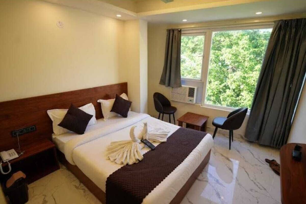 A hotel room with a large bed, a desk, a chair, and a window with curtains.