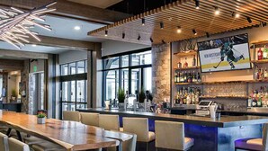 Un espace bar moderne avec une longue table en bois, des tabourets de bar et un comptoir doté d’un écran diffusant des images sur le thème du hockey.