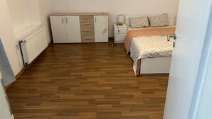 A bedroom with a wooden floor, a bed with patterned bedding, a nightstand, a dresser with drawers, and a radiator.