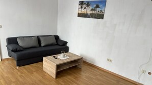A modern living room with a dark grey sofa, a wooden coffee table with a teapot, and a beach scene painting on the wall.