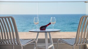Een tafel met twee wijnglazen en een fles op een balkon met uitzicht op de oceaan.
