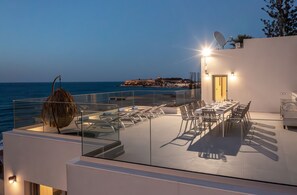A rooftop terrace with a dining area, lounge chairs, and a view of the sea.