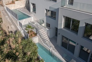 A modern multi-story building with a swimming pool, outdoor seating, and a staircase leading to a balcony.