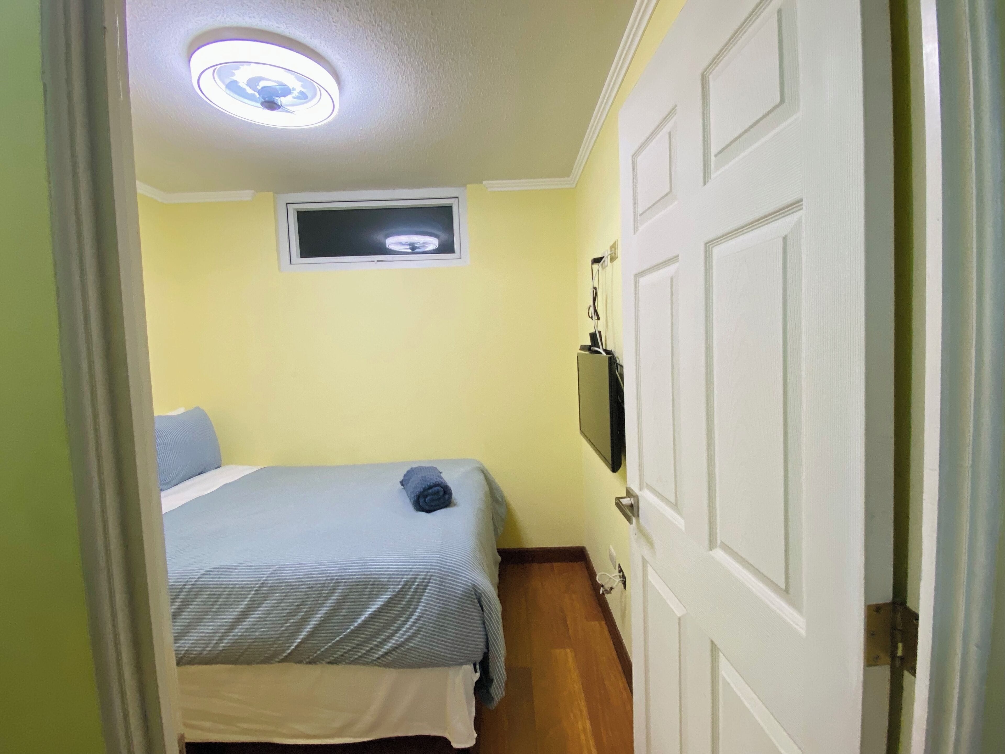 A narrow room with a bed, a television mounted on the wall, and a door.