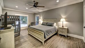 Une chambre à coucher comprenant un lit, un bureau, une chaise, une table de chevet et un ventilateur de plafond.