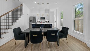 Una cocina moderna con una isla central, iluminación colgante y una escalera con barandilla.