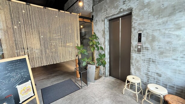 Un intérieur moderne avec un mur texturé, une cloison en bois, une plante en pot, un tableau noir servant de menu et un petit coin salon avec des tabourets.