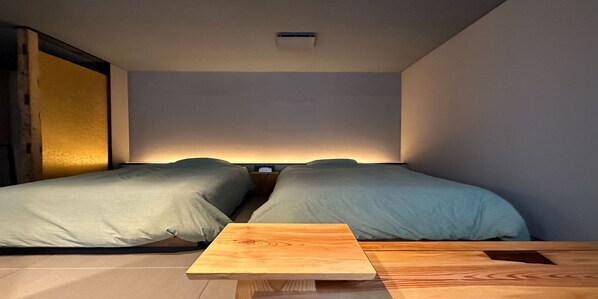 Un dormitorio pequeño y moderno con dos camas individuales, una mesita de noche de madera y una pequeña mesa.