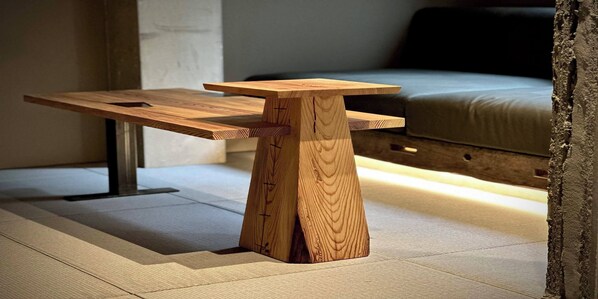A wooden table with a unique design, placed in a room with a bed and a concrete wall. - HOTEL SEN (Matsue)