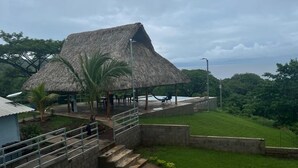 A thatched-roof structure with outdoor seating and a pathway leading to it. - Rancho Agua Fría (Jucuarán)