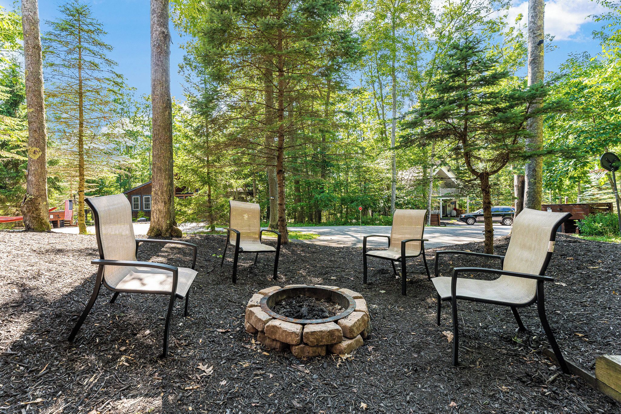 A fire pit surrounded by four chairs in a wooded area.